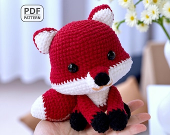 May include: A handmade crochet fox toy in red and white, with black eyes and nose. The fox is sitting, and the image includes the text "PDF PATTERN". The fox is approximately 6 inches tall.