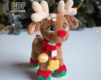 May include: A handmade brown crochet reindeer with cream-colored antlers, a red nose, and a red and white striped scarf. The reindeer has blue eyes and is wearing red and green boots. The text "PDF PATTERN" is in the upper left corner.