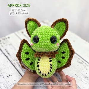 May include: A plush crochet bat toy featuring a bright green body, large black eyes, and brown-trimmed wings. The belly has a yellow and black kiwi fruit pattern. It measures approximately 7.3 by 9.25 inches. Text on image: APPROX SIZE 18.5x23.5cm (7.3x9.25inches).