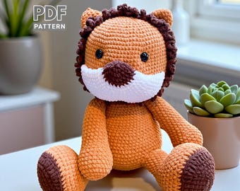 May include: A crocheted lion plush toy in shades of orange and brown, with a white muzzle and dark eyes. The lion has a brown mane and is sitting with its legs outstretched. The text "PDF PATTERN" is in the upper left corner.