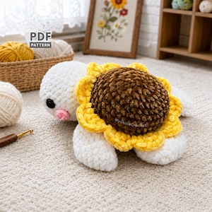 Op de afbeelding: Een handgemaakte gehaakte schildpad met een zonnebloemontwerp. De schildpad heeft een wit lichaam, een gele en bruine zonnebloem en een roze neus. De afbeelding bevat de tekst "PDF PATTERN" en de website "WyshinaCrochet".
