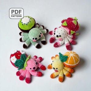 Könnte beinhalten: Eine Sammlung von vier gehäkelten Spinnen-Plüschtieren mit Früchte-Thema. Die Spinnen sind in verschiedenen Farben gehalten, darunter Grün, Rosa, Weiß und Gelb, mit Fruchtmustern wie Kiwi, Drachenfrucht, Erdbeere und Orange. Das Bild enthält ein "PDF PATTERN"-Etikett.