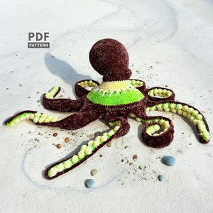 Op de afbeelding: Een handgemaakte, pluche octopus in bruin, groen en geel. De octopus heeft een getextureerd lichaam en tentakels, met een groene en gele kraag. De afbeelding bevat de tekst "PDF PATTERN" en het watermerk "WyshineCrochet".