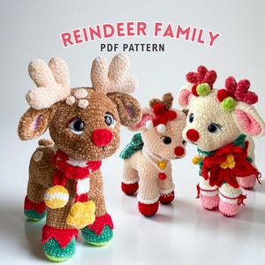 May include: Three crocheted reindeer toys in different sizes. The largest is brown with a red and white scarf and green and red details. The other two are cream-coloured with red and green details. The text "REINDEER FAMILY PDF PATTERN" is at the top.
