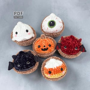 Puede incluir: Seis pequeñas figuras de peluche tejidas a ganchillo en cestas de hilo marrón, incluyendo un fantasma blanco, un globo ocular verde, una calabaza naranja, un diablo rojo con alas, un murciélago negro y un caramelo de maíz. Texto PDF PATTERN.