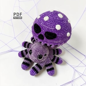 May include: A purple crochet plush toy featuring a spider with black striped legs and large black eyes, topped with a purple mushroom cap decorated with white spots and a black skull face. The image includes the text PDF PATTERN.