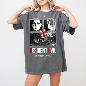May include: Gray t-shirt featuring a Resident Evil design. The graphic includes images of Ada Wong and Leon Kennedy, the Umbrella Corporation logo, and the text "RESIDENT EVIL requiem".