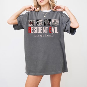 Op de afbeelding: Donkergrijs T-shirt met de tekst "RESIDENT EVIL requiem" in rood en wit. Het shirt heeft vier zwart-wit afbeeldingen boven de tekst. Het T-shirt heeft een casual, oversized pasvorm.