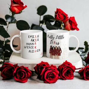 Può includere: Due tazze in ceramica bianca con testo nero e immagini. La tazza a sinistra ha un cruciverba con i nomi "Emily", "Aria", "Hanna", "Spencer" e "Alison". La tazza a destra ha il testo "Pretty Little Liars" e un'immagine di quattro donne in abiti rossi.