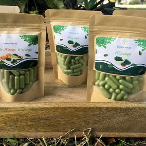 Op de afbeelding: Drie bruine papieren zakken gevuld met groene capsules. De zakken hebben etiketten met de tekst "Empath House" en verschillende productnamen: "Avocado Mango Moringa", "Moringa" en "Moringa".
