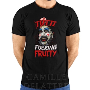May include: A black short-sleeved t-shirt featuring a graphic of a clown face with blue hair, red and white striped hat, and red cheek accents. The text above the clown reads TUTTI and below the clown reads FUCKING FRUITY in bold red and white letters.