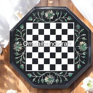 Könnte beinhalten: Achteckiges Schachbrett aus schwarzem Marmor mit einem schwarz-weißen Schachbrettmuster. Das Brett ist mit grünen und weißen floralen Designs um den Umfang herum eingelegt. Der Text "Omsaihandicraft" ist in der Mitte des Bretts sichtbar.