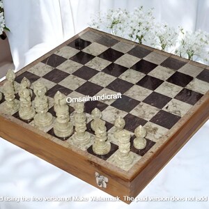 Könnte beinhalten: Ein Schachbrett aus Holz mit Marmor-Einlage und einem Satz weißer Schachfiguren. Das Schachbrett ist aus dunkelbraunem Holz gefertigt und hat eine hellbraune Marmor-Einlage. Die Schachfiguren sind aus weißem Marmor gefertigt und in der Startposition auf dem Brett angeordnet.