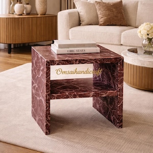 May include: A square, burgundy marble-look coffee table with a lower shelf. The table has a veined pattern and the text "Chic Stays" is on top. The text "Omsaihandicraft" is on the front of the table. The table is in a living room setting.
