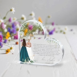 May include: A heart-shaped acrylic keepsake with a floral design and two women in wedding attire. The text reads "To my Maid of Honor on my Wedding Day". The text continues with a message of appreciation for the maid of honor and is signed "Love, Sophia" with a date.