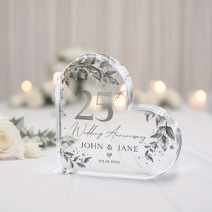 May include: A clear heart-shaped crystal paperweight with a silver design. The paperweight features the number 25, the words "Wedding Anniversary", the names "JOHN & JANE", and the date "09.18.1999".