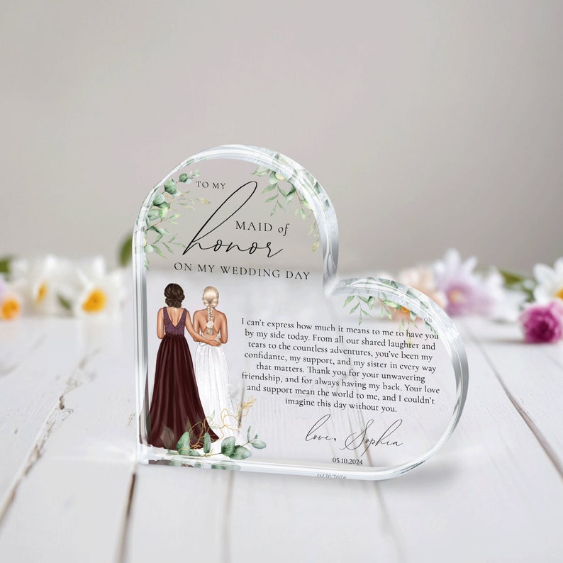 May include: A heart-shaped glass keepsake with a floral design and a message to a maid of honor. The text reads "To my Maid of Honor on my Wedding Day." The message continues with a heartfelt sentiment about the importance of the friendship and support of the maid of honor. The text is signed "Love, Sophia" and dated "05.10.2024".