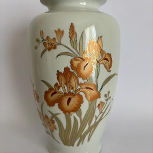 May include: A white ceramic vase with a gold rim and a floral design featuring orange and gold irises on a white background.