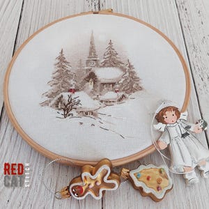 May include: A cross-stitch embroidery of a winter village scene in a wooden hoop, with a church and snow-covered trees. Includes gingerbread man and cookie ornaments, and a small angel figurine.