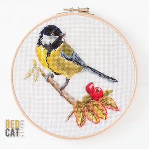 Könnte beinhalten: Kreuzstich-Stickerei eines gelben und schwarzen Vogels, der auf einem Zweig mit roten Beeren sitzt. Der Vogel ist von Herbstblättern umgeben. Die Stickerei ist in einem Holzreifen gerahmt.