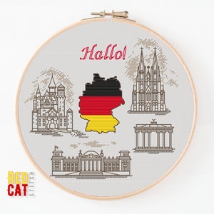 Puede incluir: Un patrón de punto de cruz con monumentos alemanes icónicos, incluyendo el Castillo de Neuschwanstein, la Catedral de Colonia, la Puerta de Brandeburgo y el edificio del Reichstag. El patrón también incluye la bandera alemana y la palabra "¡Hola!" en rojo.