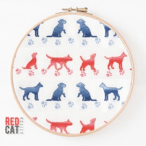 May include: A white embroidery hoop with a red and blue dog pattern. The dogs are in a repeating pattern and are outlined in black. The hoop is made of wood and has a natural finish.
