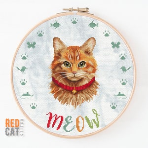 May include: Cross-stitch pattern of an orange tabby cat with a red collar and the word "MEOW" in colorful letters. The cat is surrounded by a circle of paw prints, butterflies, and birds.