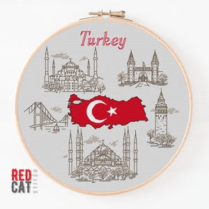 Può includere: Un telaio da ricamo a punto croce con una mappa della Turchia rossa, con una mezzaluna e una stella bianche, e disegni a tratteggio di monumenti. La parola "Turkey" è in corsivo rosso. Il logo Red Cat Stitch è in basso.