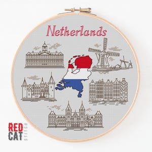 May include: A cross-stitch embroidery hoop featuring a design of the Netherlands. The design includes the word "Netherlands" in red, a map of the country in red, white, and blue, and illustrations of landmarks like windmills and buildings.