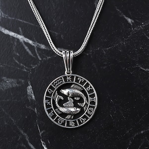 Op de afbeelding: Zilveren ketting met een ronde hanger met het sterrenbeeld Vissen, twee in elkaar verweven vissen, omringd door de astrologische tekens van de dierenriem.