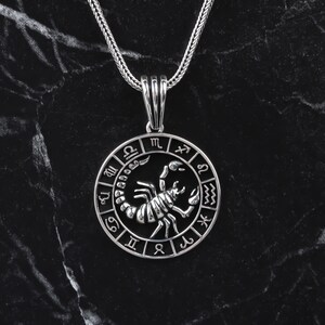 Op de afbeelding: Zilveren ketting met hanger met een schorpioen sterrenbeeld met een cirkel van sterrenbeeld symbolen eromheen.