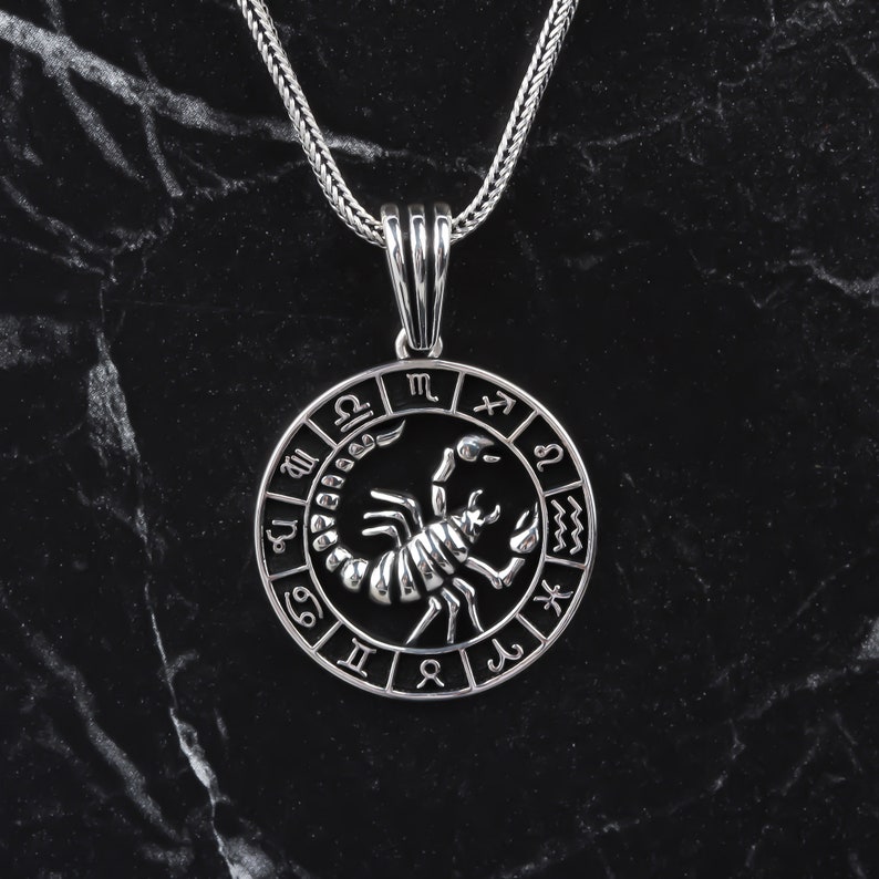 Op de afbeelding: Zilveren ketting met hanger met een schorpioen sterrenbeeld met een cirkel van sterrenbeeld symbolen eromheen.