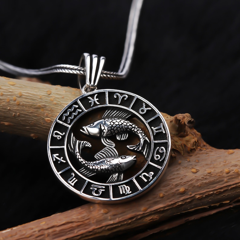 Op de afbeelding: Zilveren ketting met hanger met een cirkelvormige dierenriem met de astrologische tekens en twee zilveren vissen, die het sterrenbeeld Vissen voorstellen.