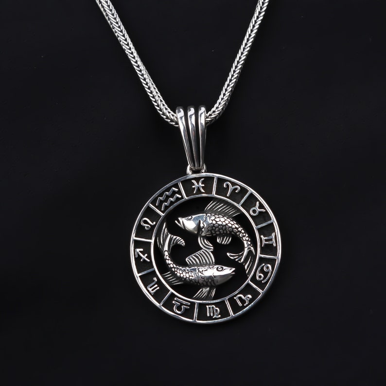 Op de afbeelding: Zilveren ketting met een ronde hanger met het sterrenbeeld Vissen, twee vissen en de astrologische tekens van de dierenriem.
