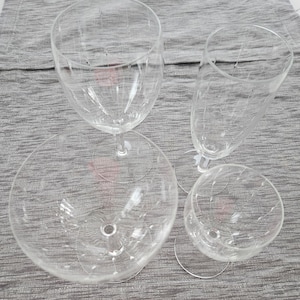 May include: Four clear, stemmed glasses with etched designs. The set includes a large wine glass, a champagne flute, a small wine glass, and a wide-bowled glass. The glasses are arranged on a gray textured surface.