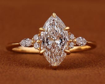 May include: A gold engagement ring featuring a large, pear-shaped diamond as the centerpiece. The ring is accented with smaller diamonds on either side of the main stone, set on a gold band. The ring is displayed against a brown background.