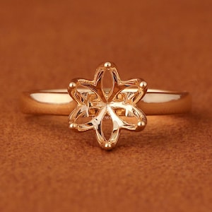 May include: A polished gold-tone ring featuring a six-prong setting shaped like a flower or star. The band is smooth and circular, connecting to the central decorative mount which is designed to hold a gemstone in the center of the petals.