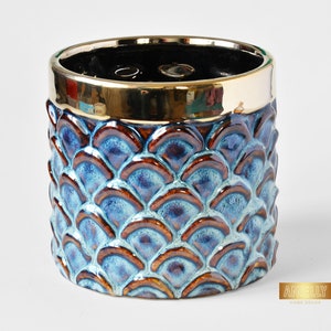 Puede incluir: Una maceta de cerámica azul y marrón con un borde dorado y un patrón de escamas. La maceta mide aproximadamente 15 cm de alto.