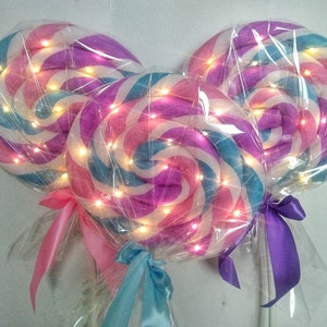 Puede incluir: Tres grandes decoraciones de piruletas de espiral de colores con luces blancas. Las piruletas son rosas, azules y blancas con envoltorio de plástico transparente. Cada piruleta tiene un palo blanco y una cinta a juego.