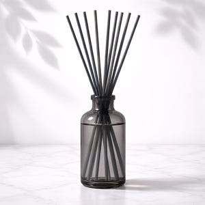 May include: A gray glass aromatherapy diffuser bottle with dark gray reeds. The bottle is filled with a clear liquid and sits on a white marble surface. The background has a soft leaf shadow.