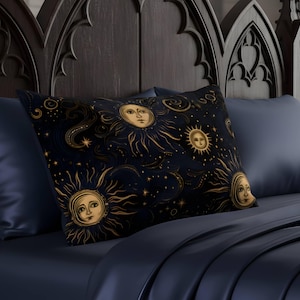 May include: A rectangular decorative pillow with a celestial design featuring sun faces, stars, and swirling patterns in gold against a dark blue background. The pillow is placed on a bed with dark blue sheets and pillows, with a dark wooden headboard.