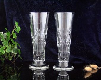 May include: Two clear glass beer glasses with a diamond pattern etched into the glass. The glasses have a wide base and a tall, slender body.