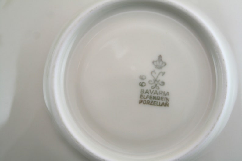 May include: Close-up of the underside of a white porcelain plate with a gold logo that reads "Bavaria Elfenbein Porzellan".