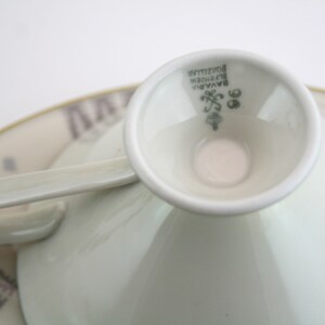 May include: Close-up of the base of a white porcelain teacup with a green mark that reads "Bavaria,  Porzellan,  Rosenthal,  98".