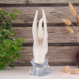 May include: White porcelain swan figurine with outstretched wings, standing on a blue and white base that resembles water waves.
