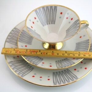 May include: A set of three white porcelain teacups and saucers with a geometric pattern in shades of grey and red. The cups and saucers have a gold trim.