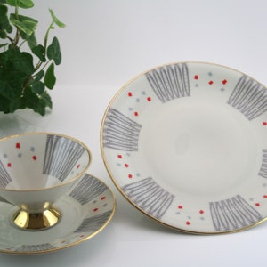 May include: A vintage teacup and saucer set with a grey and red geometric pattern. The cup and saucer have a gold rim.