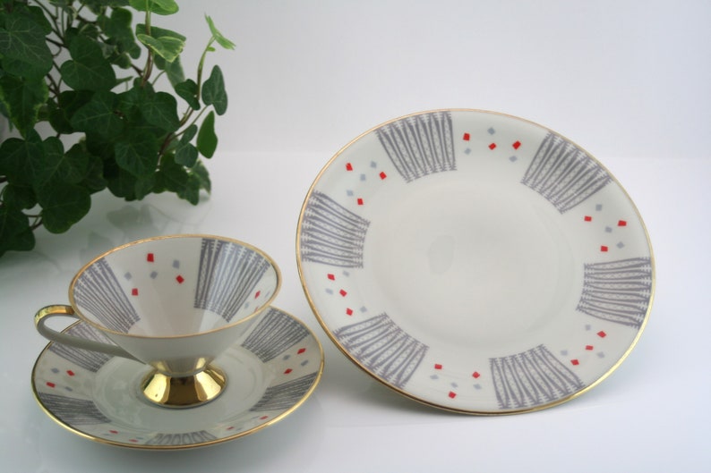 May include: A vintage teacup and saucer set with a grey and red geometric pattern. The cup and saucer have a gold rim.