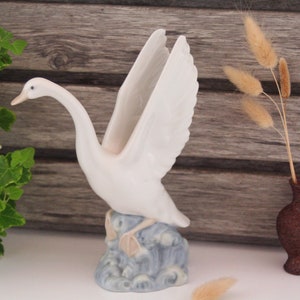 May include: White porcelain swan figurine with outstretched wings, standing on a blue and white wave base.