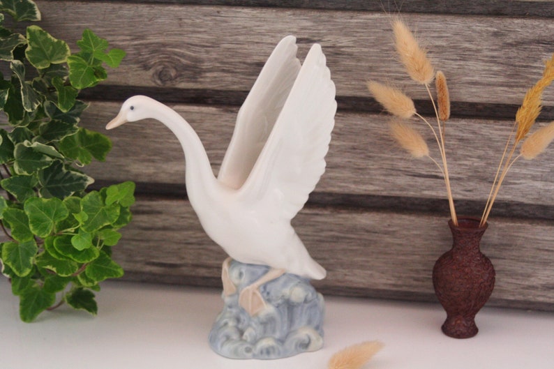 May include: White porcelain swan figurine with outstretched wings, standing on a blue and white wave base.